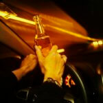 Car driver holds an alcoholic beverage while driving at night