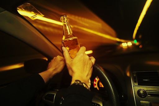 Car driver holds an alcoholic beverage while driving at night
